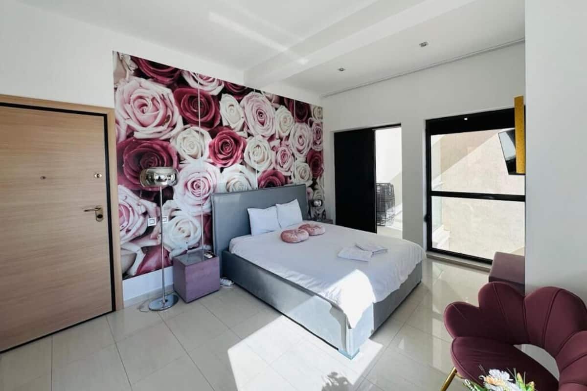 Un dormitorio moderno con una cama grande, una mesita de noche, una lámpara de pared y vistas al exterior a través de un amplio ventanal.