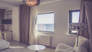 Una habitación de hotel moderna con cama, escritorio, silla, mesa redonda, televisión, ventana con vista al mar y una araña.
