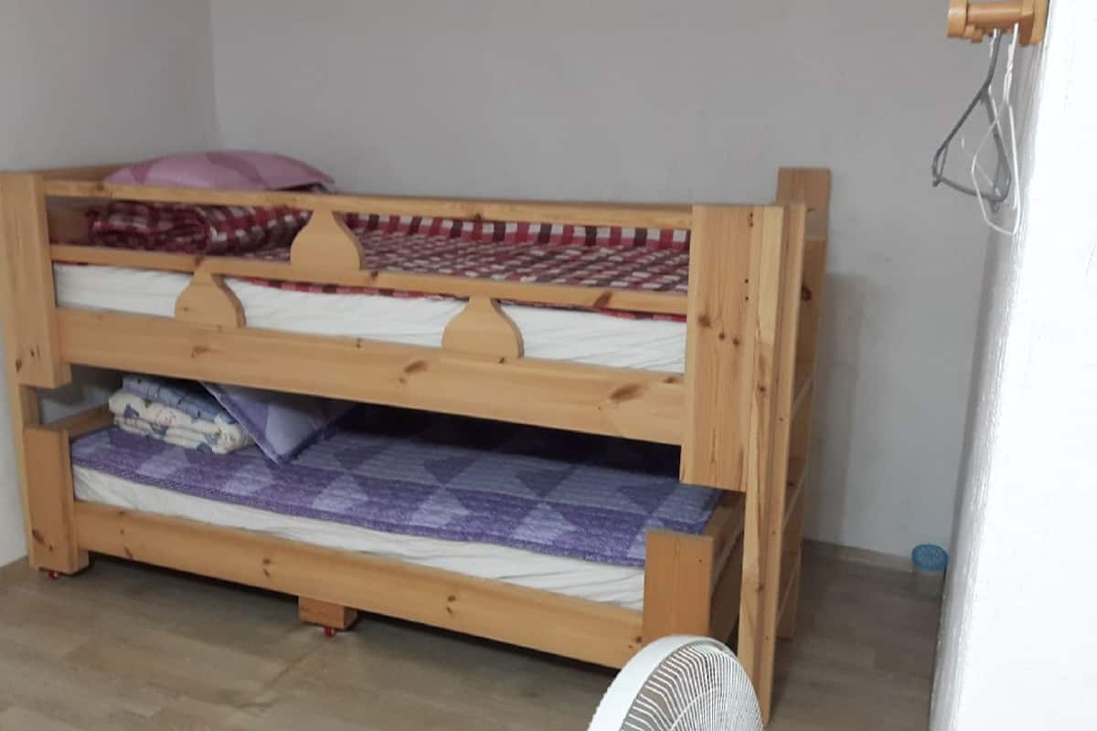 Un lit superposé à deux niveaux, avec une structure en bois et un matelas recouvert d’une couverture à carreaux.