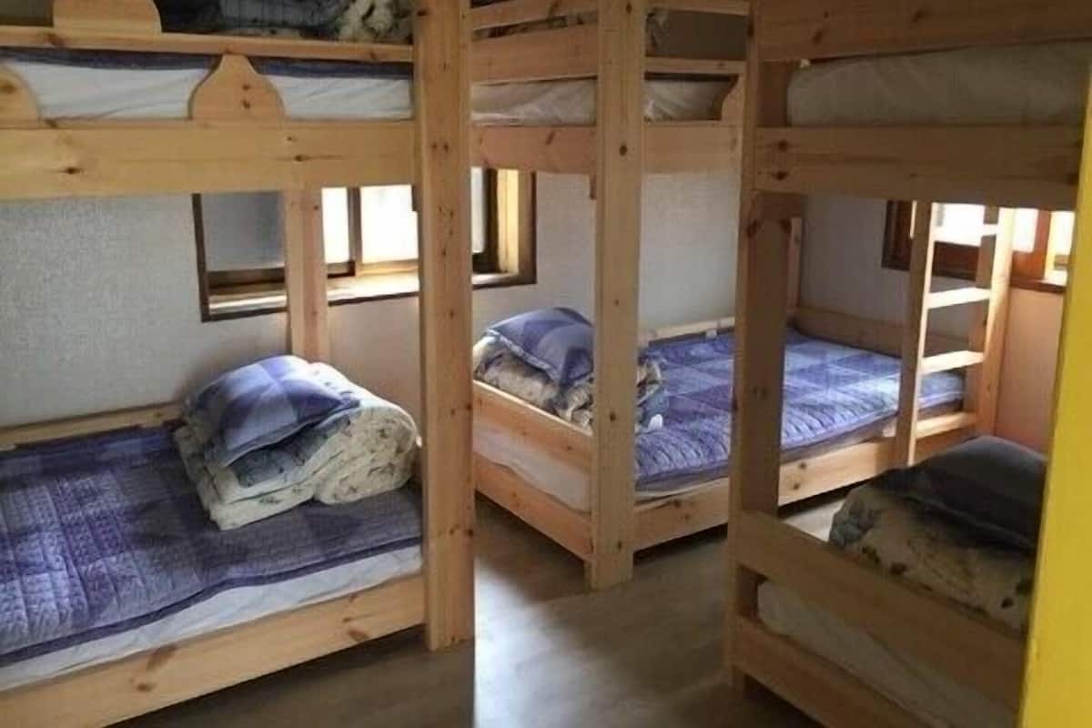 Une chambre avec trois lits superposés en bois, chacun étant équipé d’un matelas et d’oreillers.