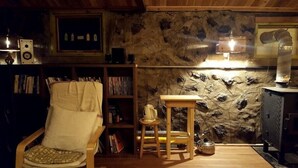 Una habitación acogedora con pared de piedra, una silla de madera, una mesita con tetera y una estantería.