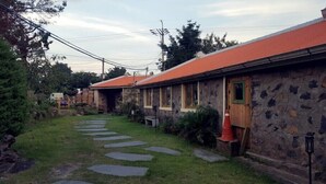 Un edificio de piedra con techo rojo, un camino de piedra que lleva a la entrada y una pequeña área ajardinada.