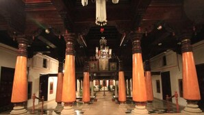 A grand hallway with high wooden columns, a checkered floor, and a chandelier. - Chidambara Vilas - A Luxury Heritage Resort (Thirumayam)