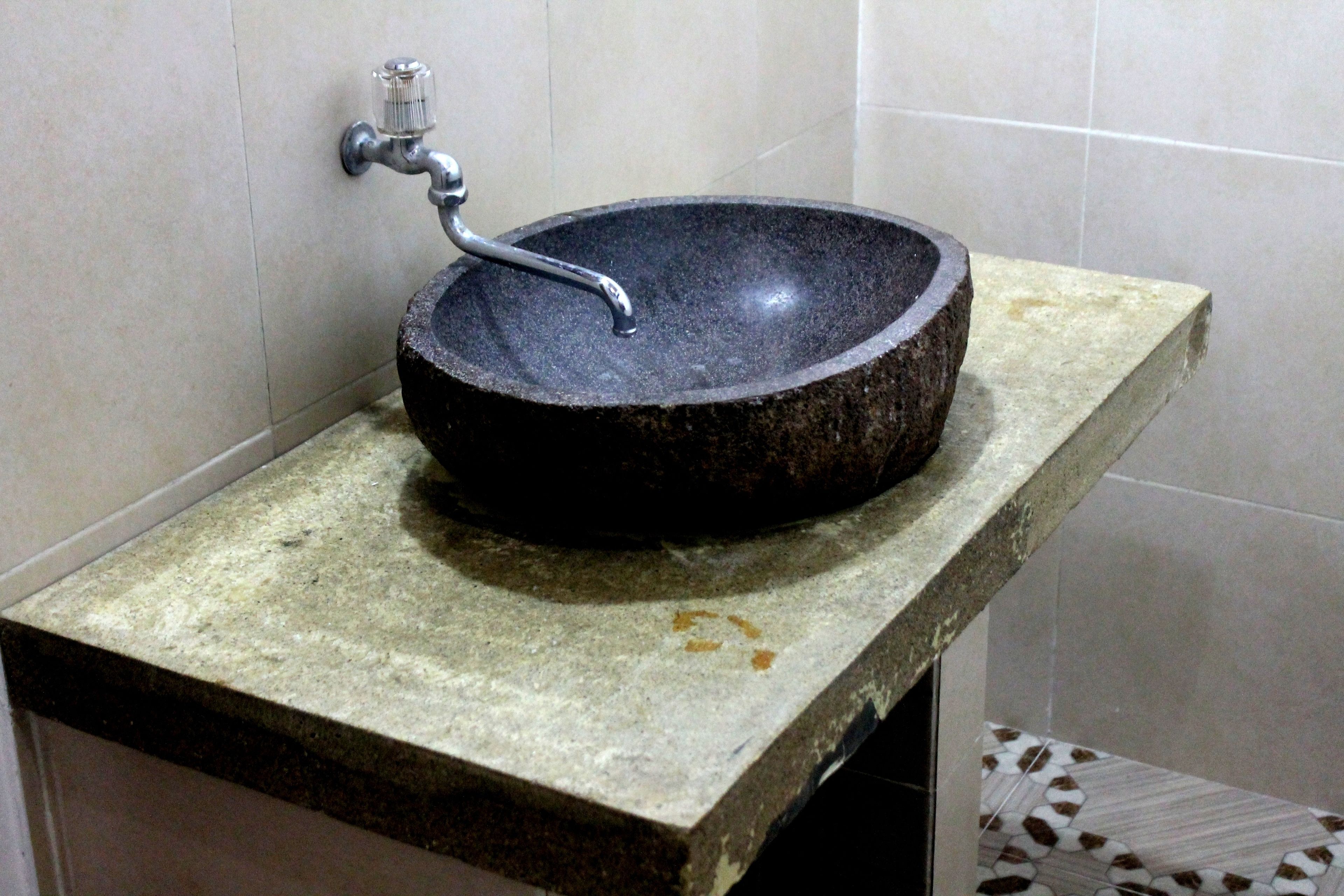 A stone sink with a metal faucet in a bathroom with tiled walls and floor.