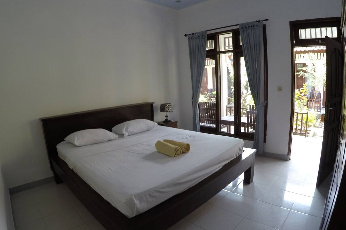 Une chambre à coucher avec un grand lit, une table de chevet et une vue sur l’extérieur grâce à une porte-fenêtre coulissante.