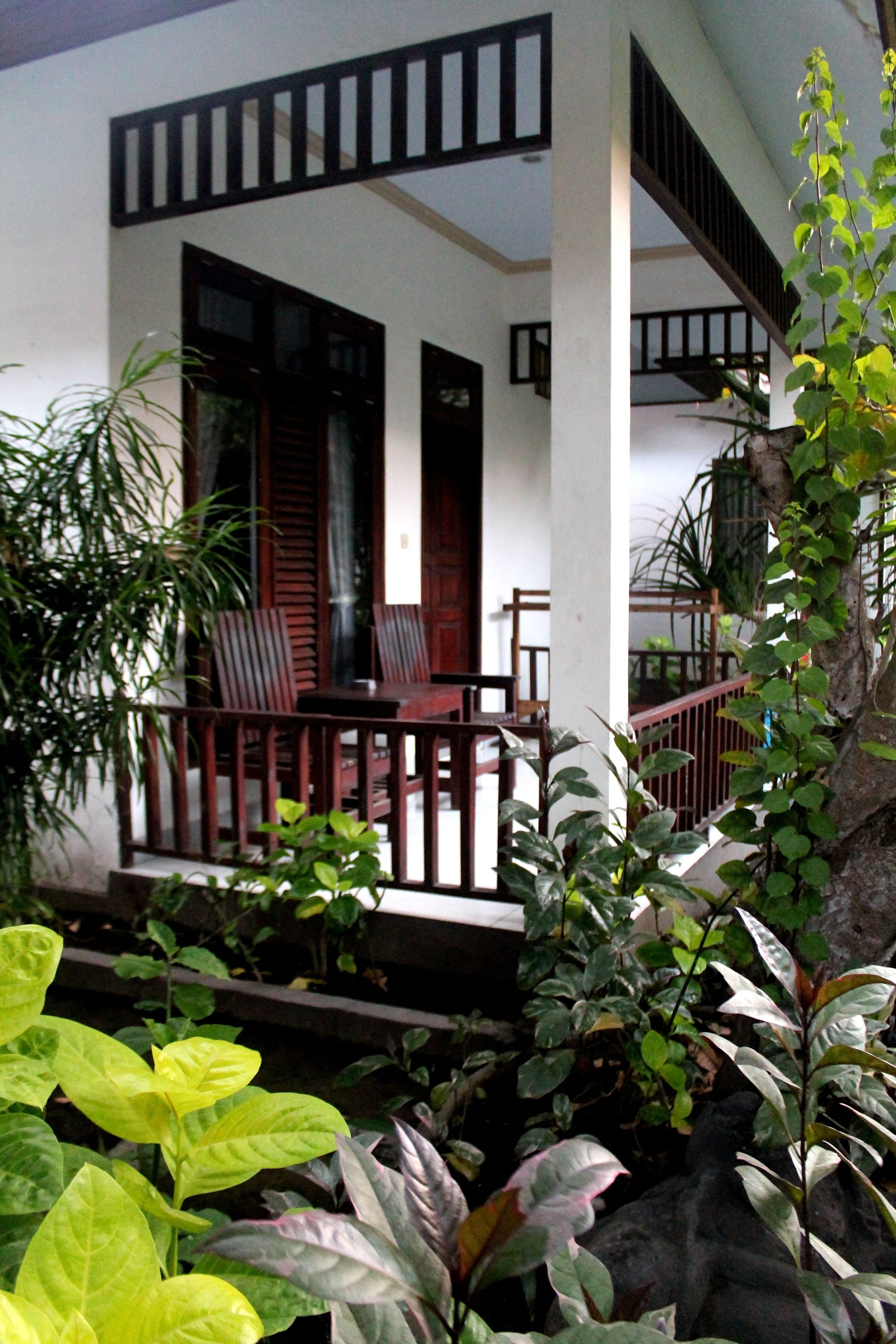 A traditional house with a wooden porch, a staircase, and a garden area with various plants.