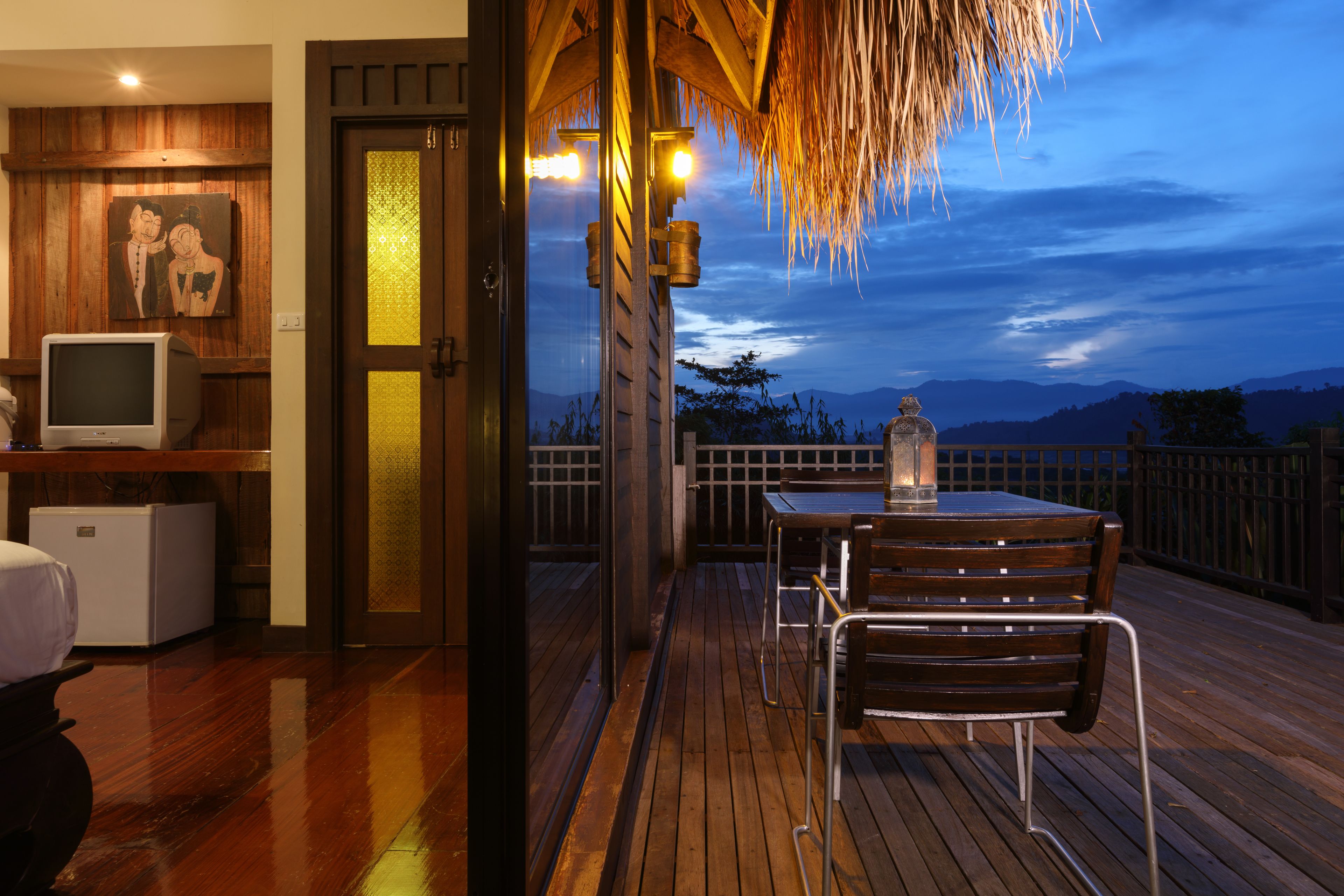 A wooden deck with a table and chairs, a television, and a refrigerator.