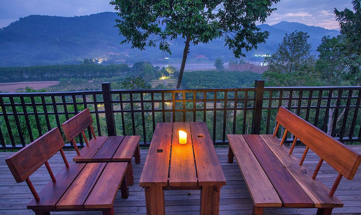 A wooden deck with benches and a table, overlooking a mountainous landscape with a fence and trees.