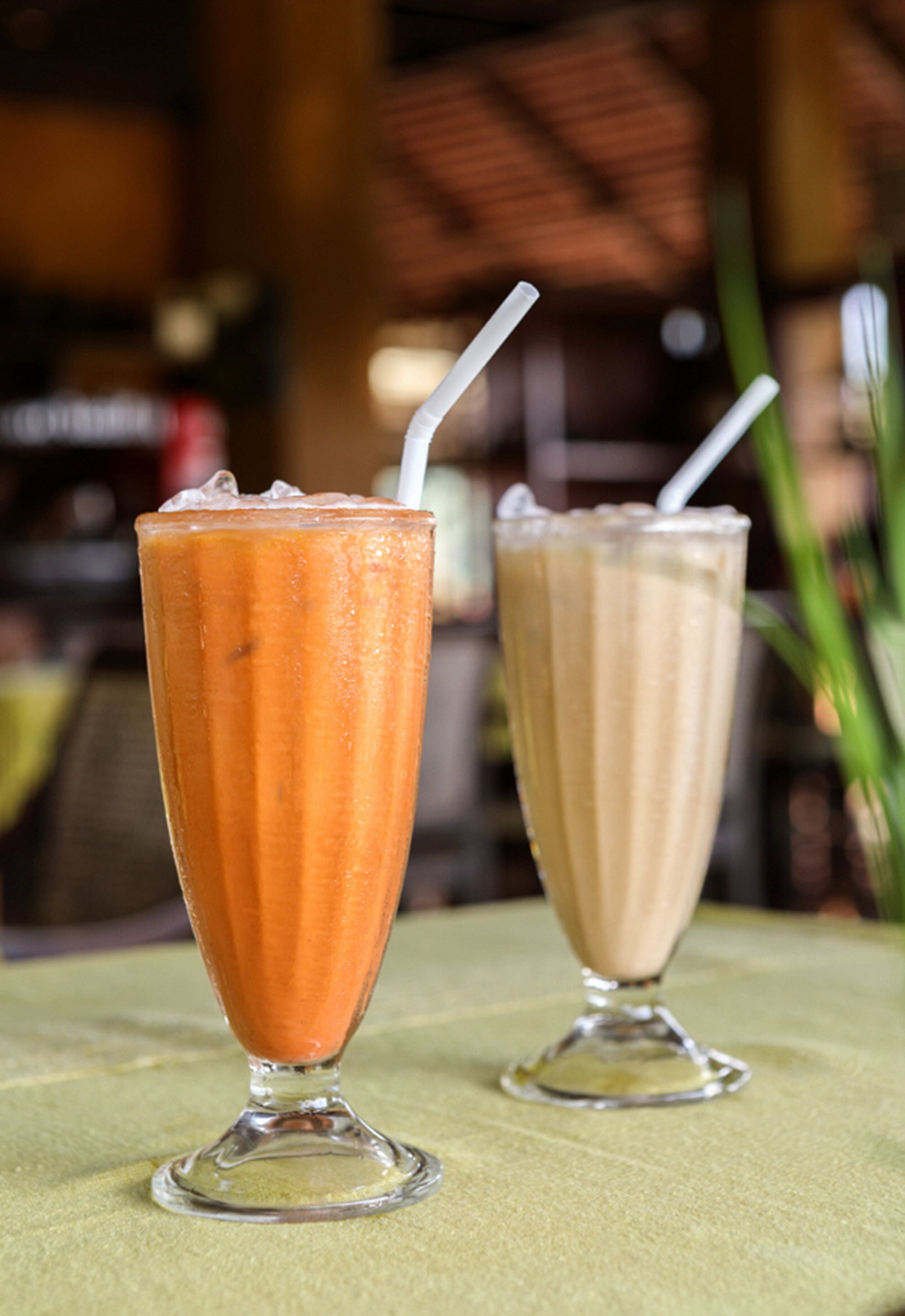 Two tall glasses of iced drinks with straws, placed on a table with a green cloth.