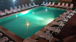 Una piscina con múltiples tumbonas alrededor.