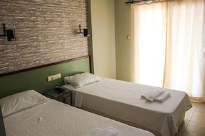 Una habitación de hotel con dos camas individuales, una pared de ladrillo, un cabecero verde, una mesita de noche y una ventana con cortinas.