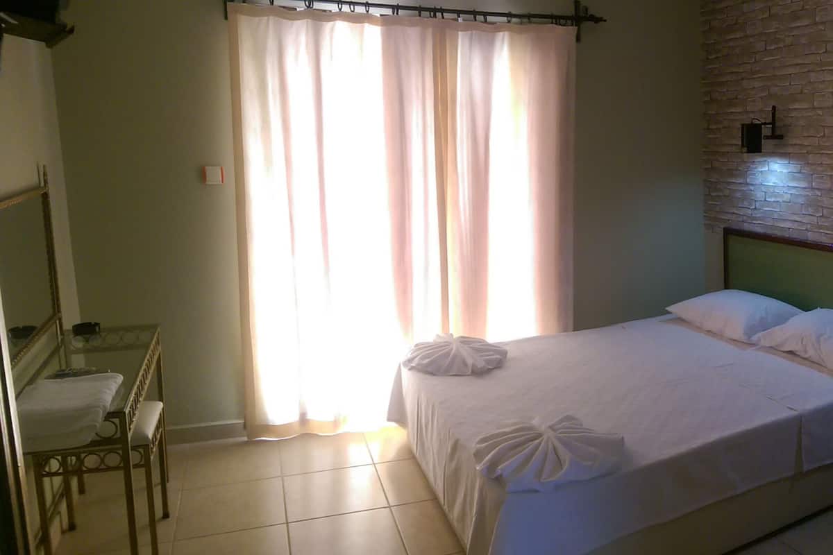 Quarto bem arrumado com uma cama, uma cadeira, uma mesinha e uma janela com cortinas.
