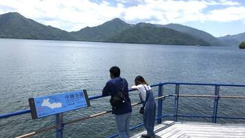 A wooden dock with a railing, a sign indicating Lake Chuzenji, and a view of the lake and mountains.