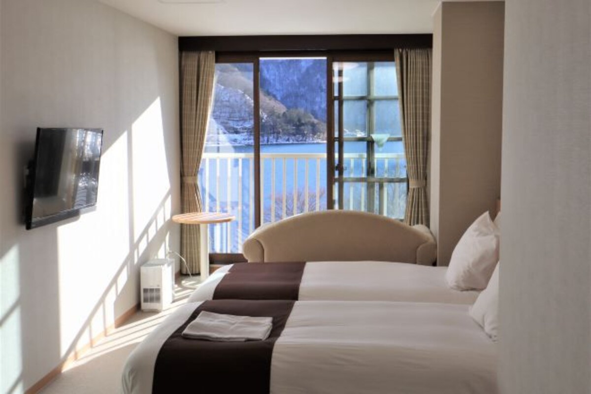 A hotel room with a bed, a TV, a window with a view of mountains, and a balcony.