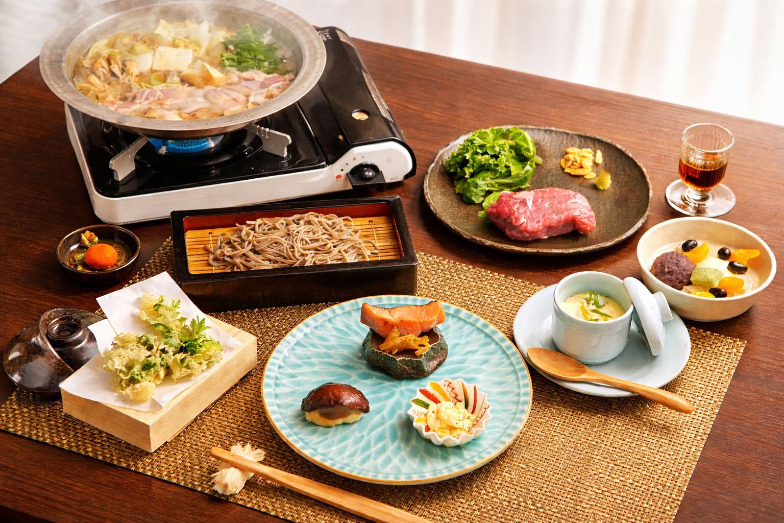 Una comida japonesa tradicional con una olla caliente, varios platos y una taza de té.