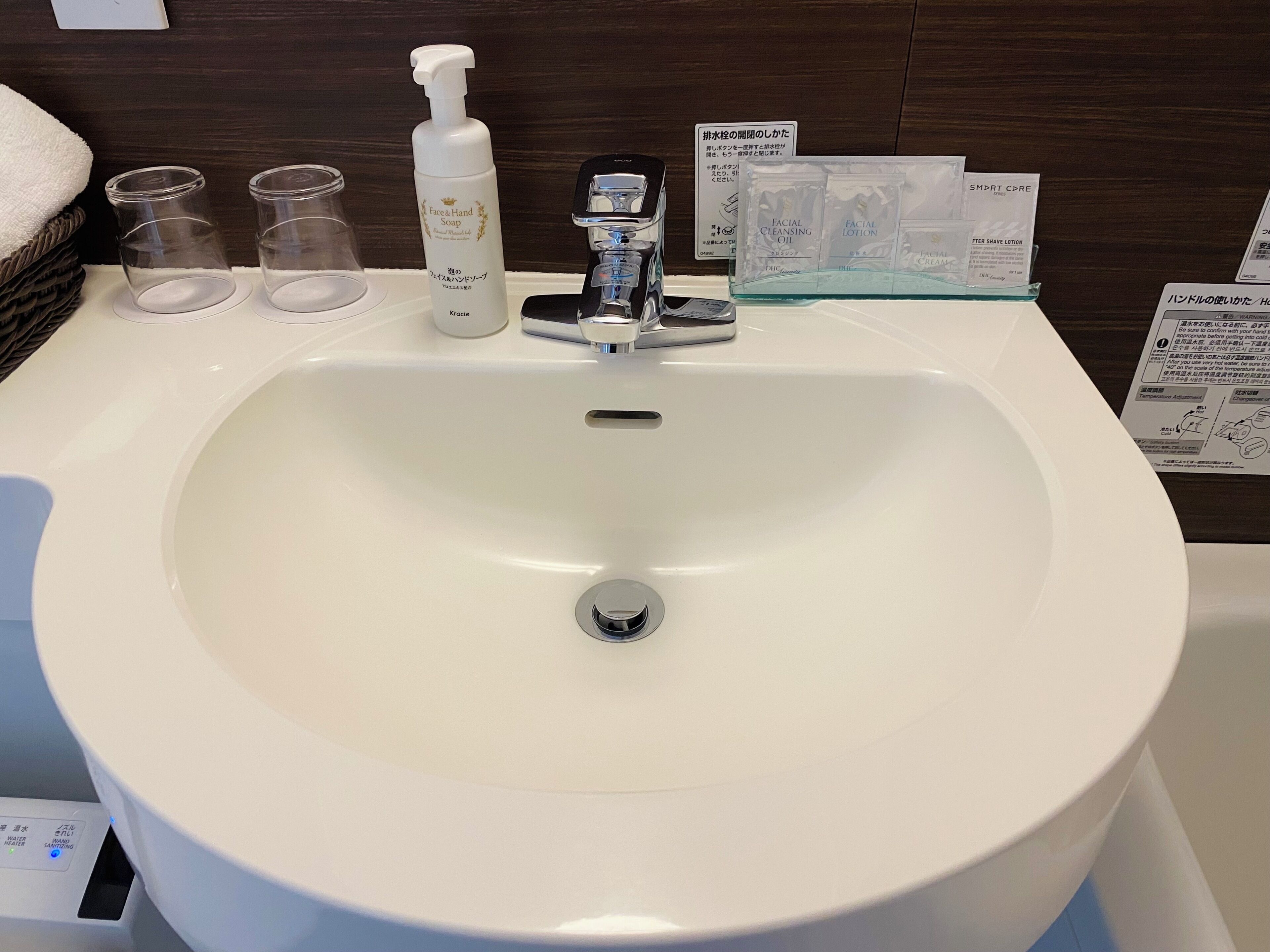A white bathroom sink with a chrome faucet, a bottle of hand soap, and a glass of water.