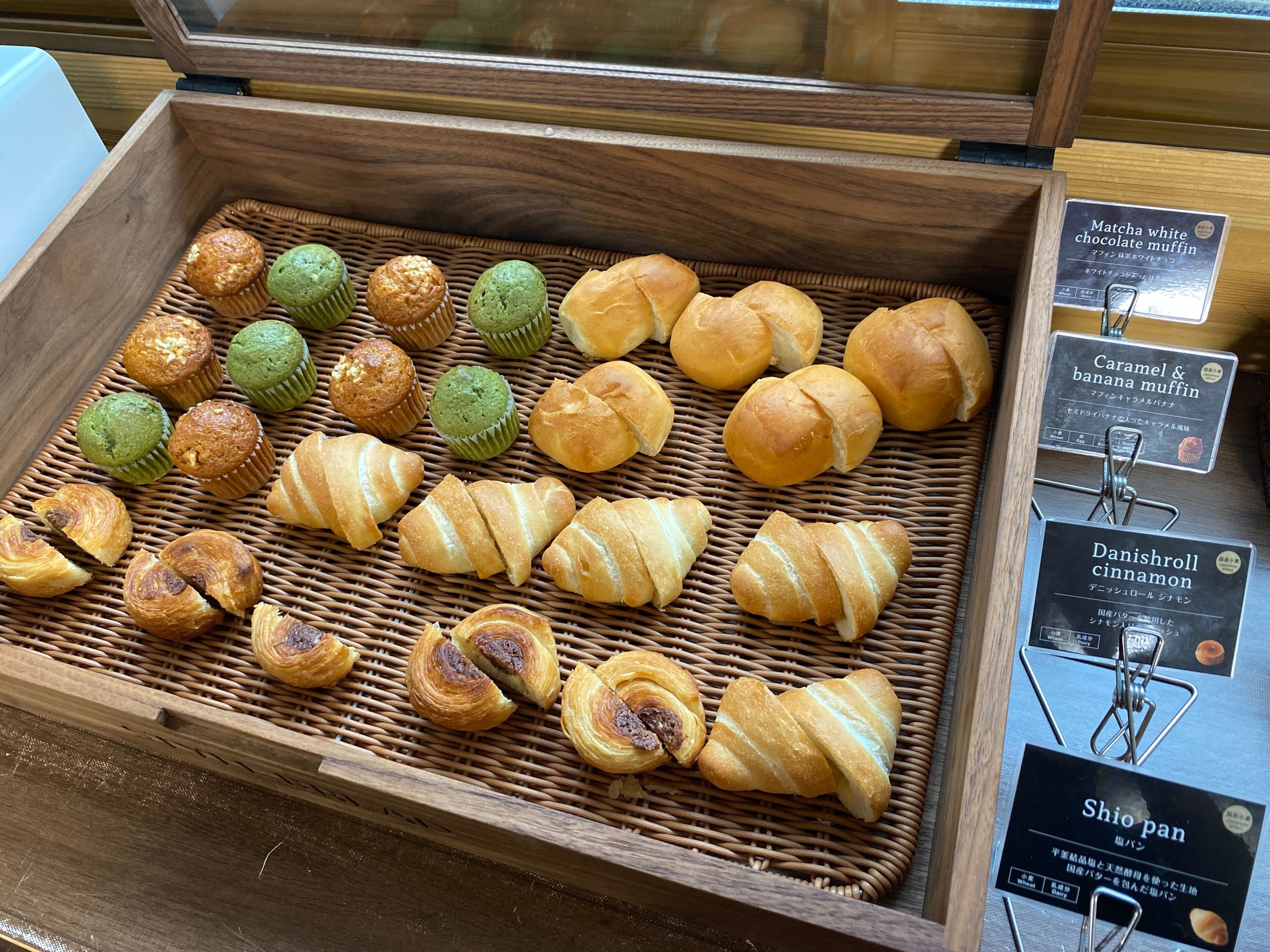 A wooden display case with various baked goods, including muffins and croissants.
