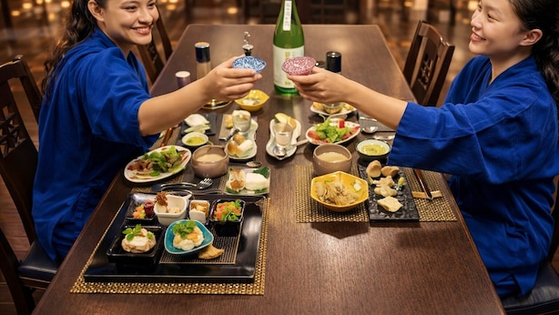 Una mesa de comedor con diferentes platos, una botella y dos personas vestidas de azul.