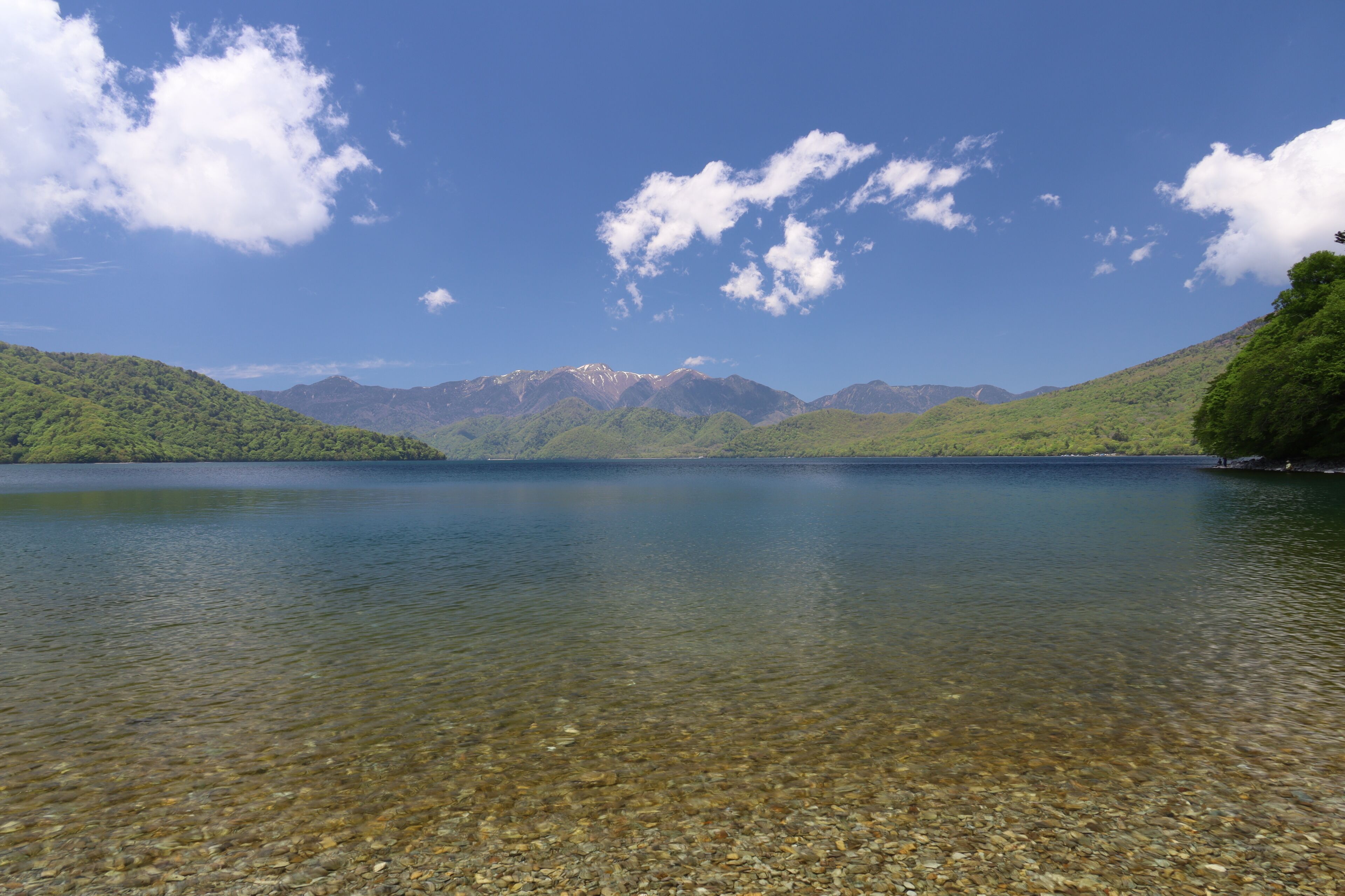 Ein klarer See mit Bergen im Hintergrund und blauem Himmel.