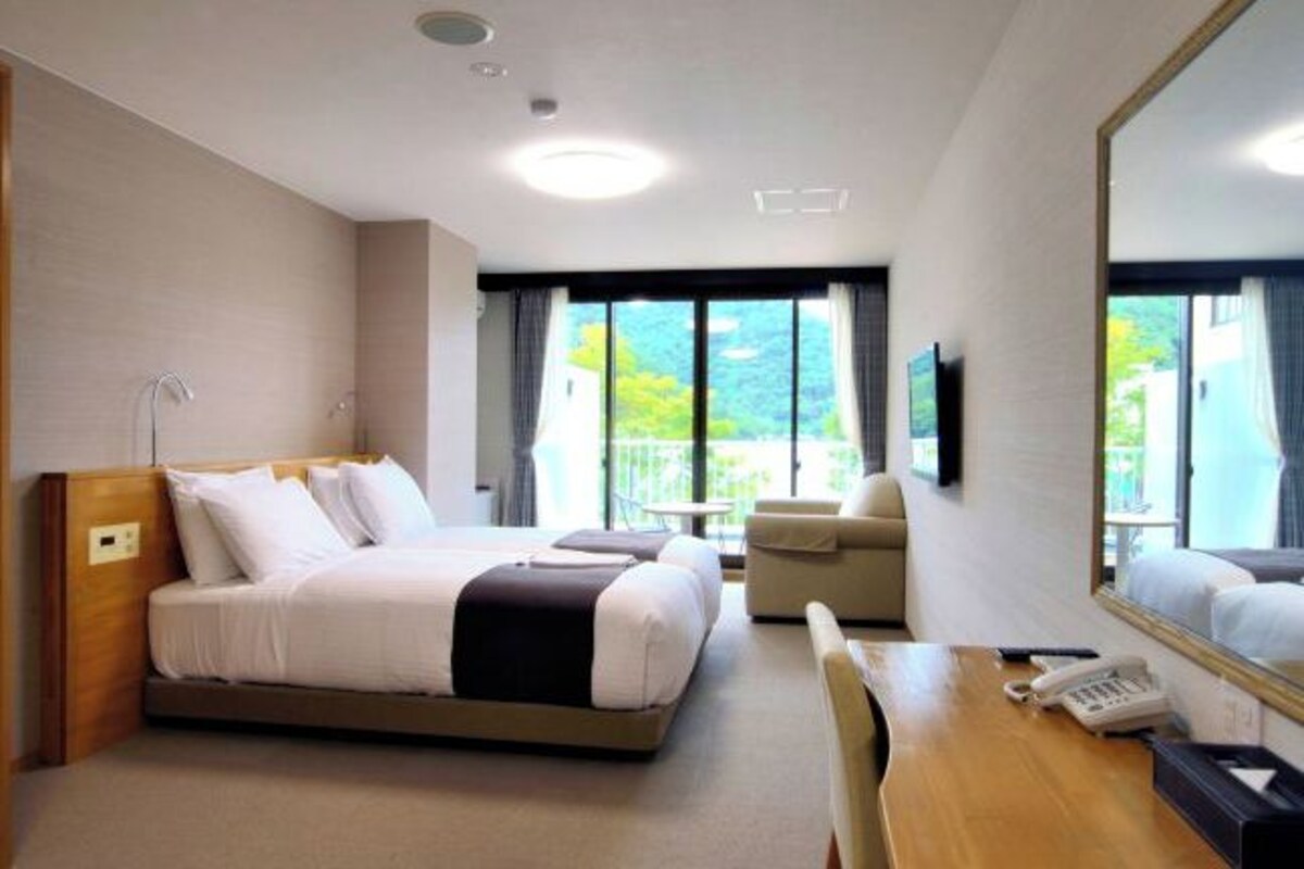 A hotel room with a bed, a desk, a chair, a phone, and a large window with a view.