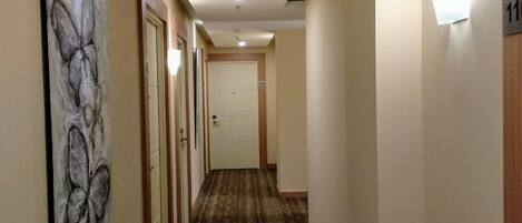 A hotel hallway with a patterned carpet, a butterfly artwork on the left wall, and a door with the number 11 on it.