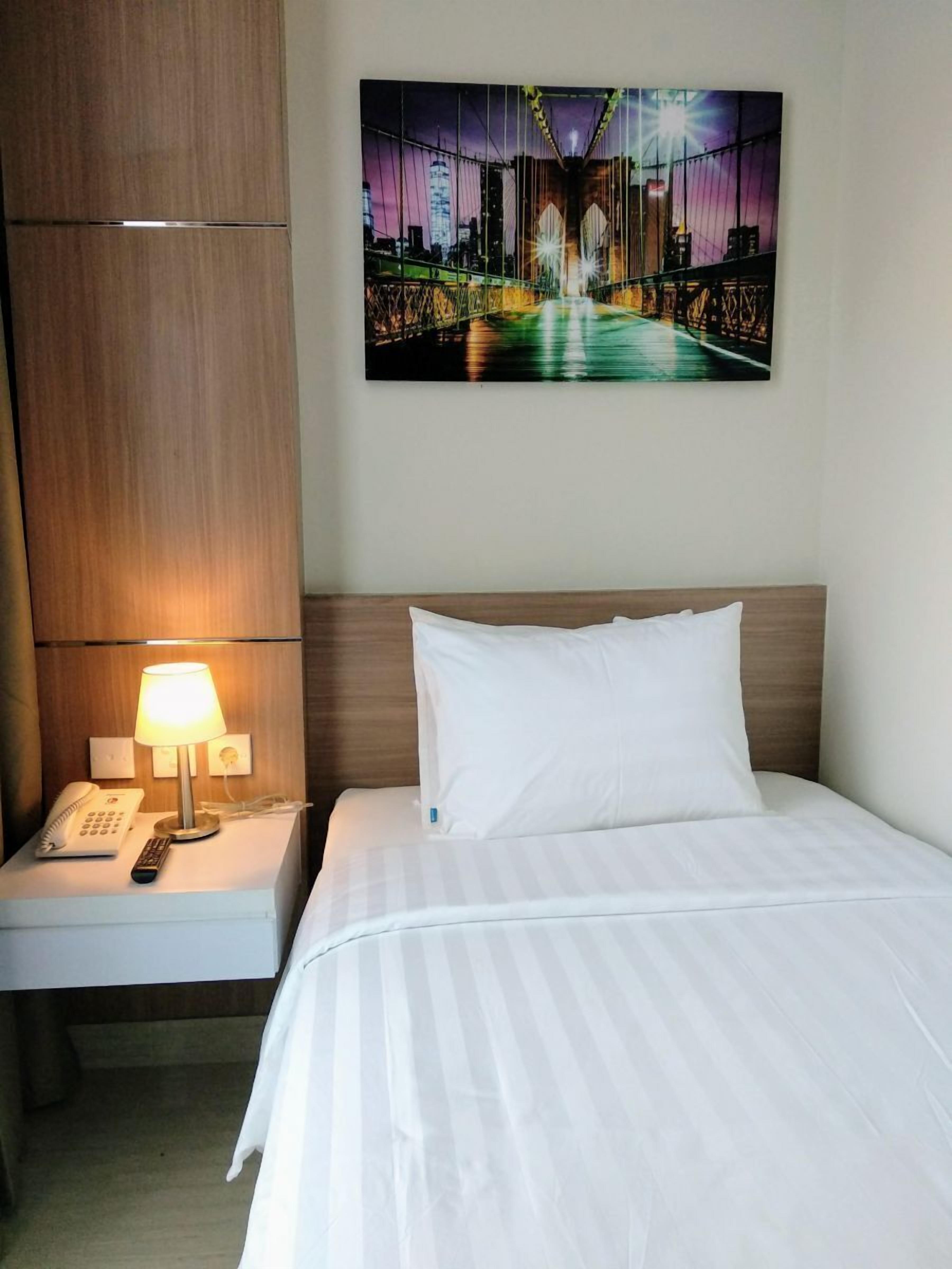 Habitación de hotel con cama, mesita de noche con lámpara, teléfono y un cuadro de un puente.