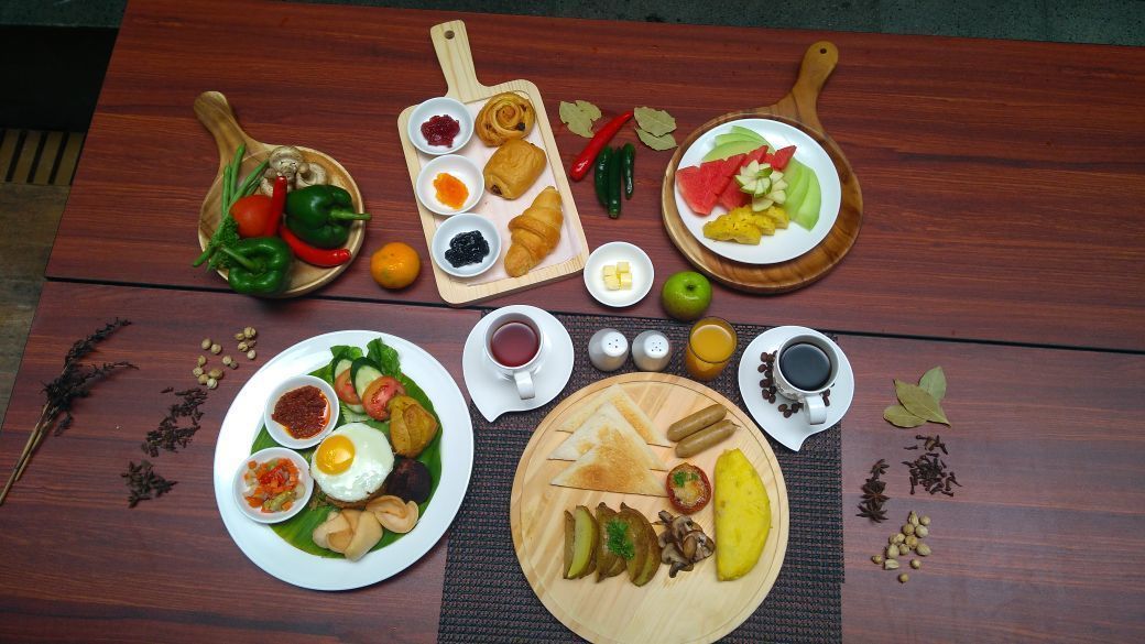 Una mesa de madera con diversos alimentos para el desayuno, incluyendo frutas, verduras, huevos y salsas.
