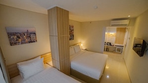 Habitación de hotel con dos camas, un cuadro de paisaje urbano, un equipo de aire acondicionado y un espejo que refleja la habitación.