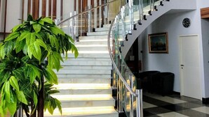 Una escalera moderna con barandillas de vidrio, una planta en maceta y una lámpara decorativa.