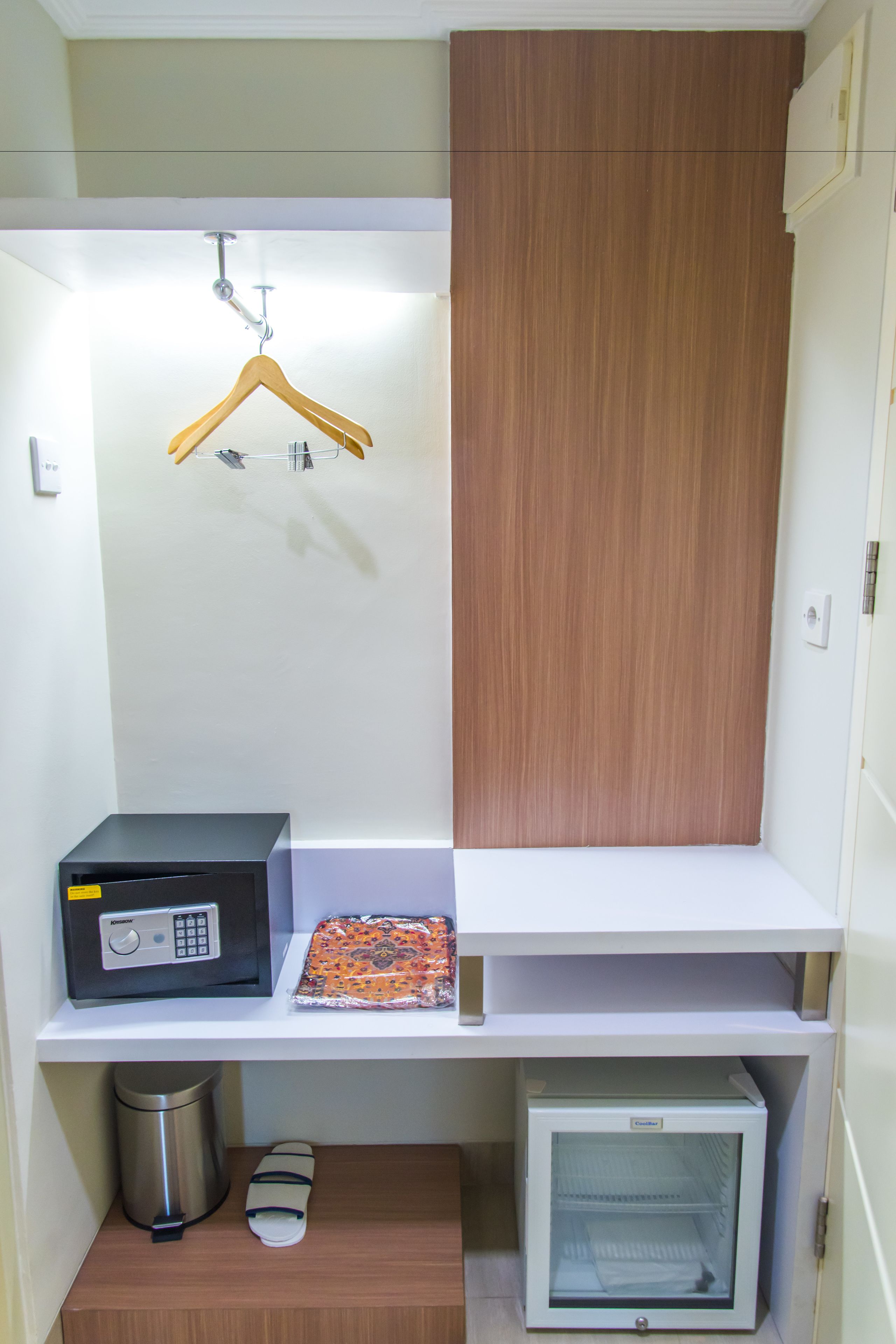 Quarto compacto com micro-ondas, mini-geladeira, cabideiro e armário de madeira.