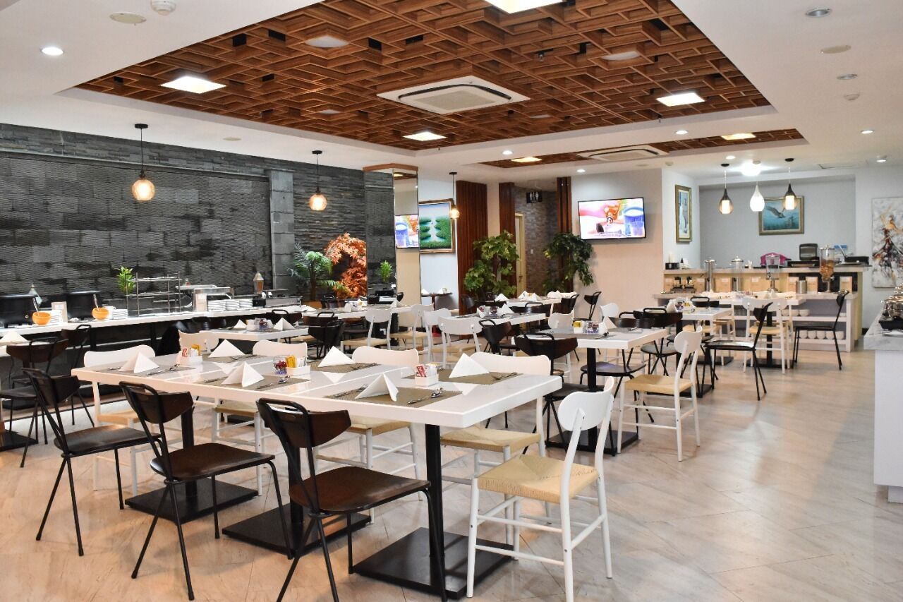 Un comedor amplio con varias mesas y sillas, un diseño de techo moderno y una zona de cocina al fondo.