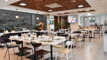 A spacious dining area with multiple tables and chairs, a modern ceiling design, and a kitchen area in the background.