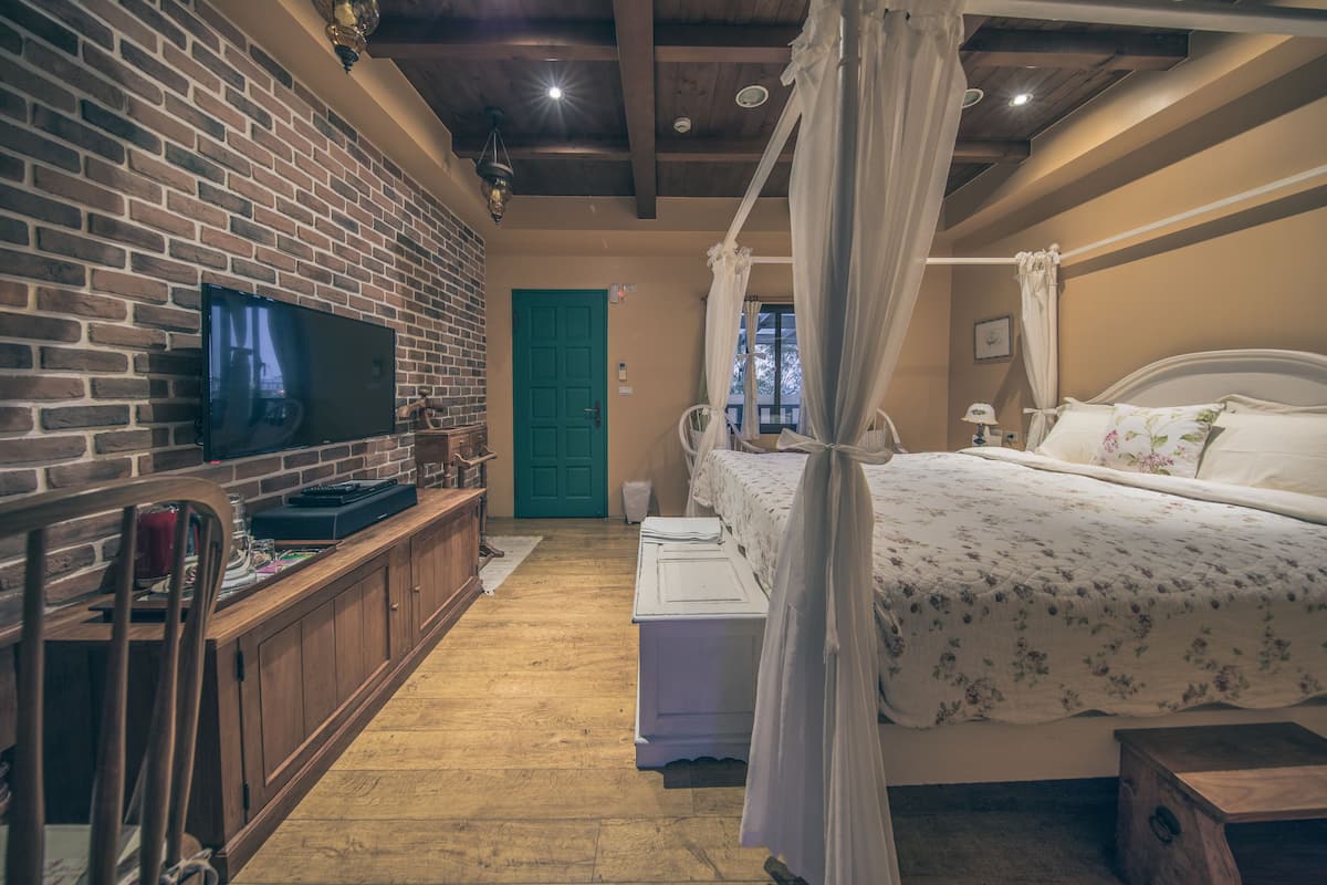 Un dormitorio con pared de ladrillo, televisor, cama con dosel y banca de madera.