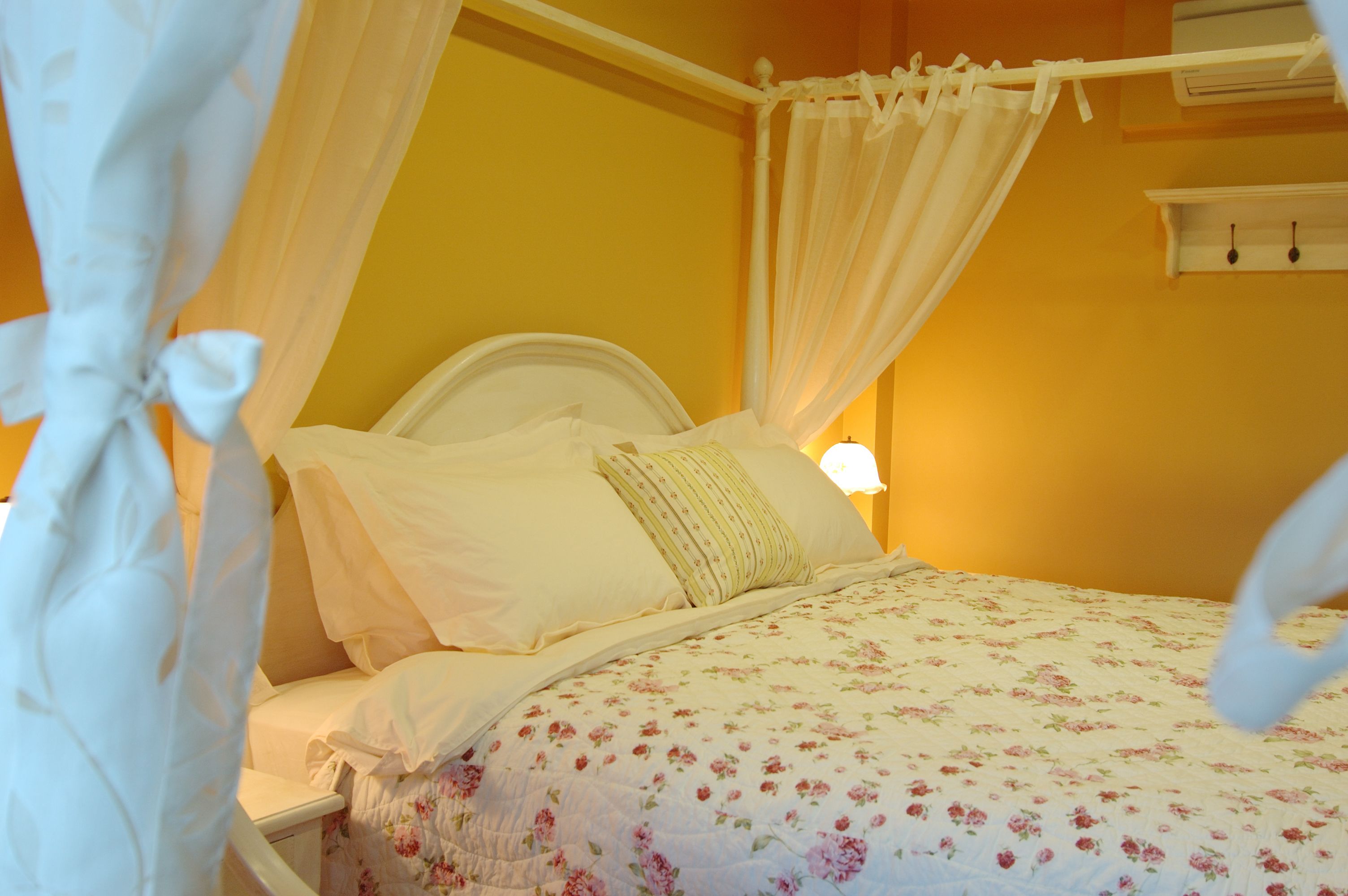 A bed with a canopy, a bedside table, and a wall-mounted shelf with two hooks.
