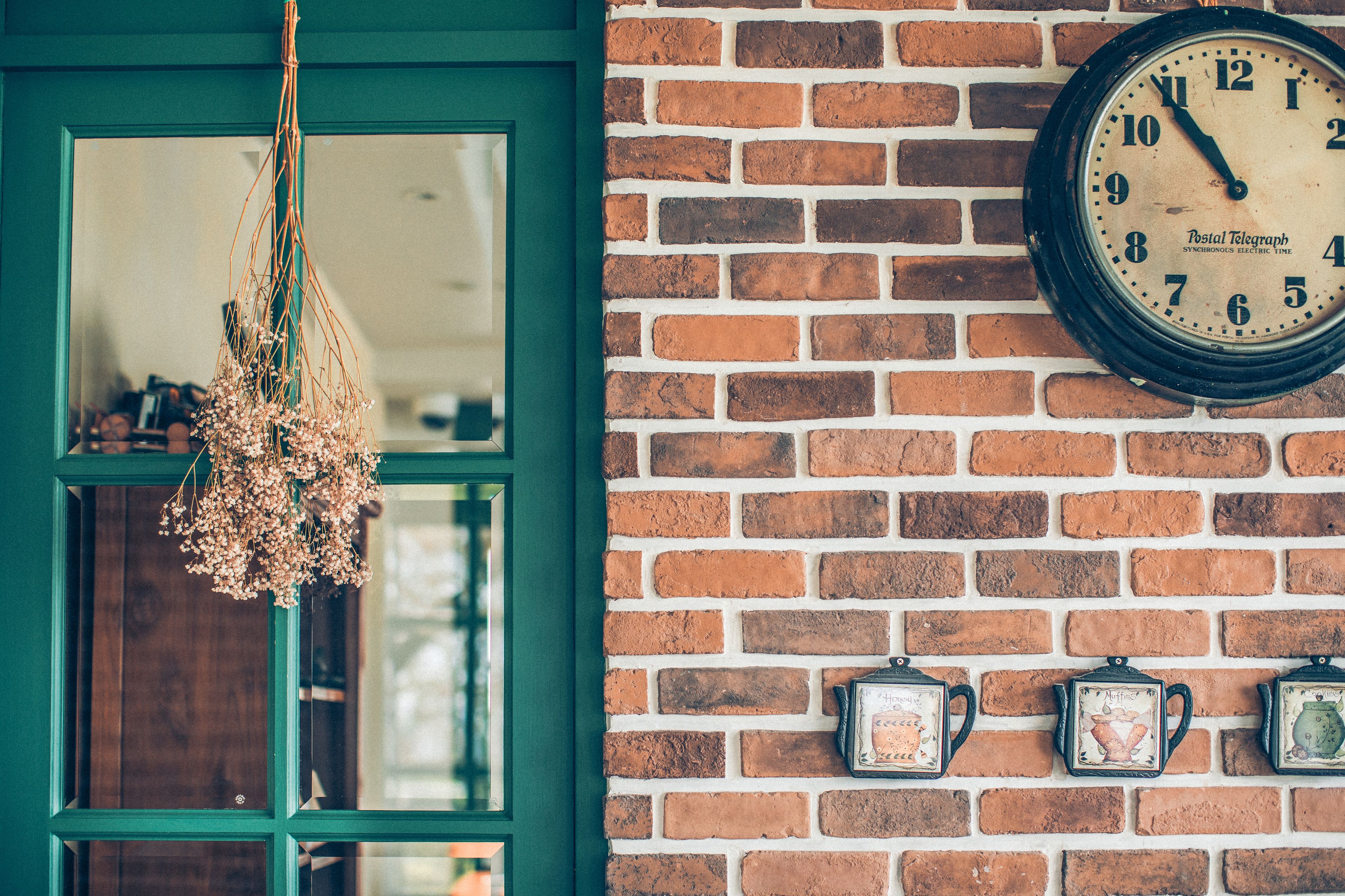 A brick wall with a clock and three teapots.