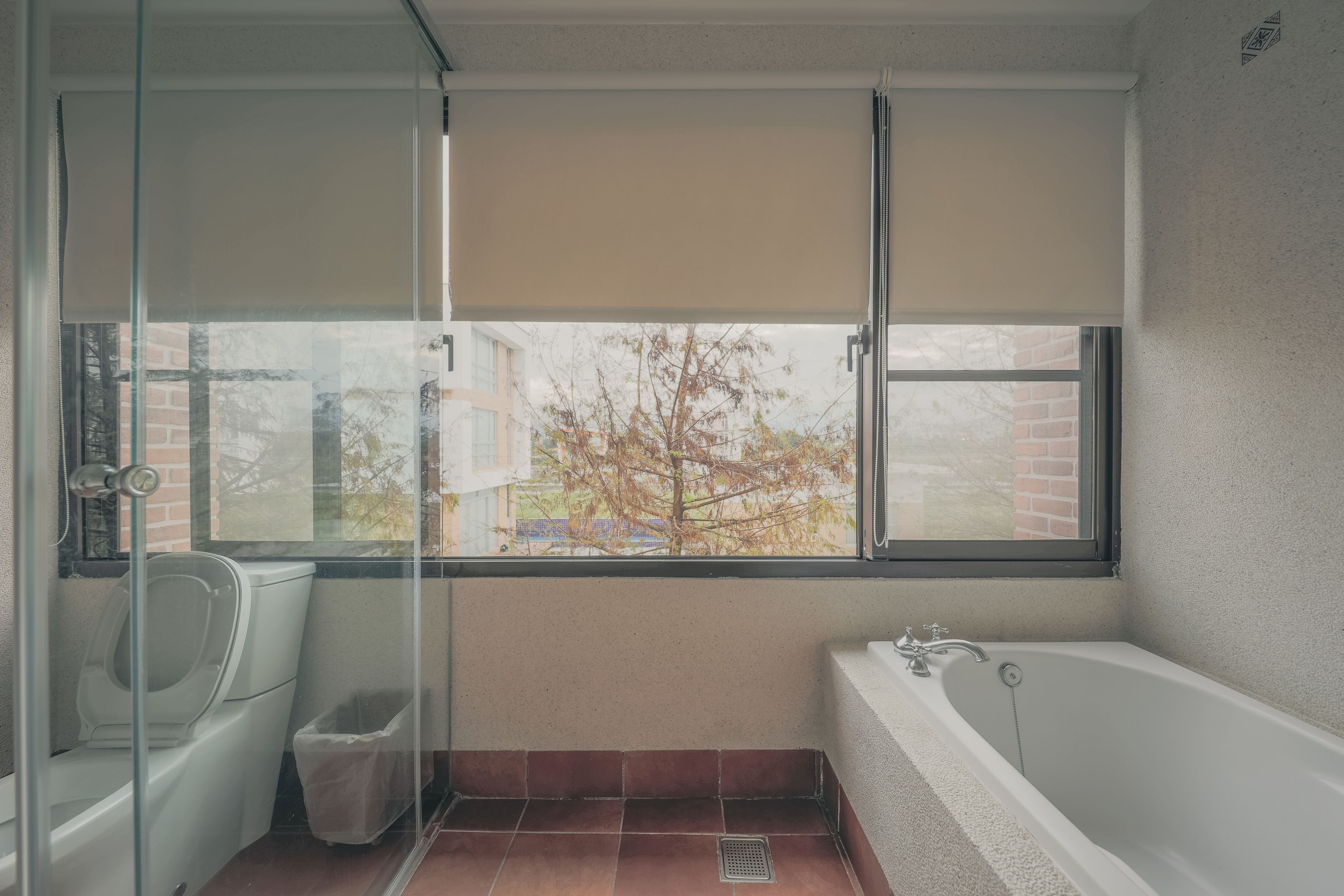 A bathroom with a bathtub, a toilet, and a shower. There is a window with a view of trees and buildings.