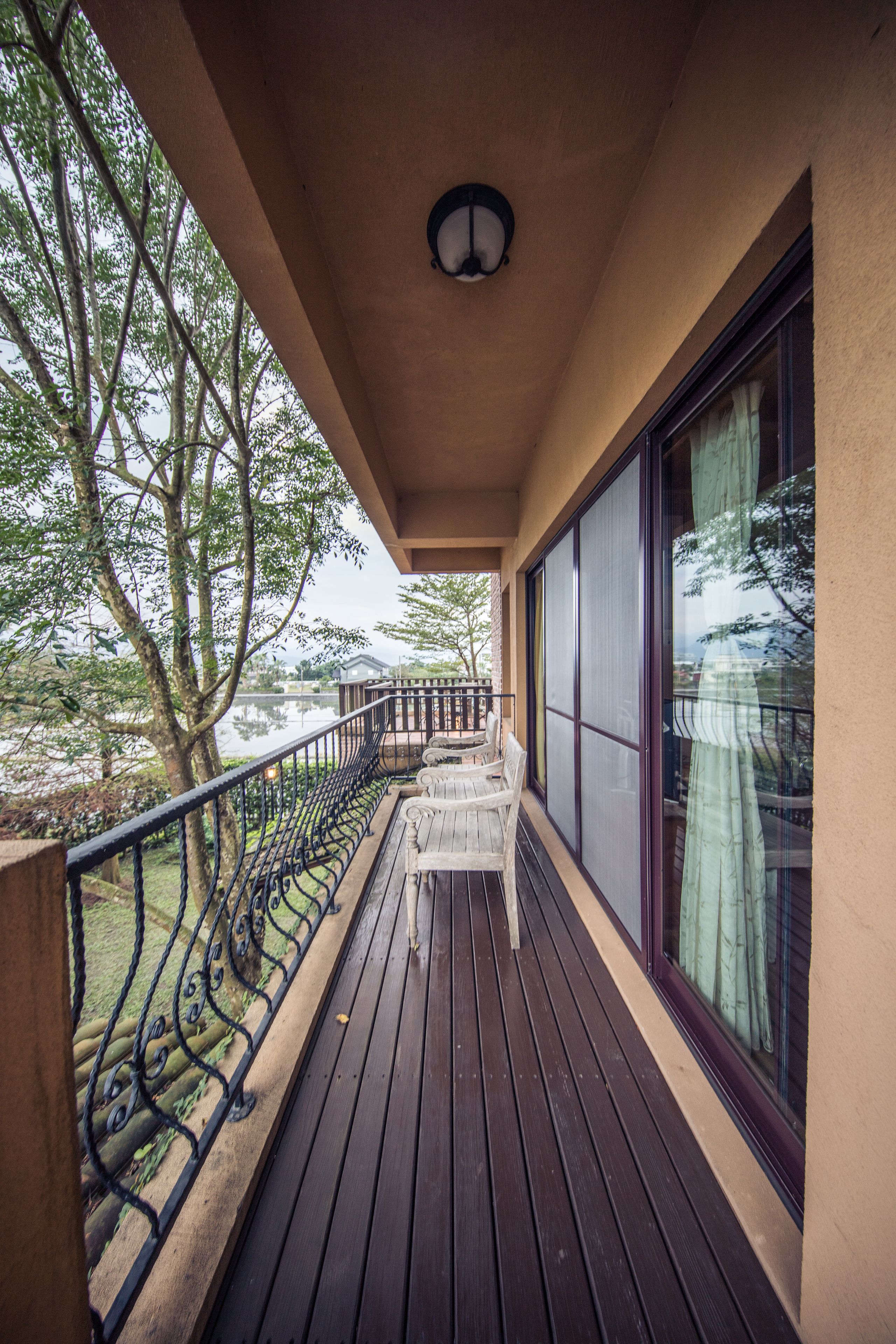 Um deck de madeira com guarda-corpo, mesa e cadeiras, com vista para a água e árvores.