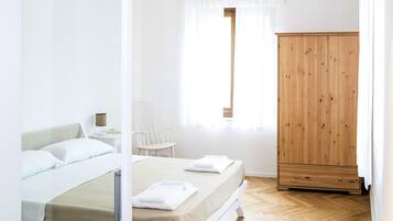 Un dormitorio con cama, armario de madera, una silla y una ventana con cortinas.