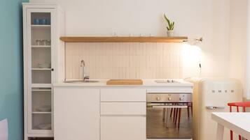 A compact kitchen with white cabinetry, a wooden countertop, a built-in oven, and a vintage refrigerator.