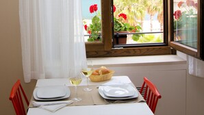 A dining table set with plates, glasses, and a basket of bread, overlooking a balcony with a view of the sea and palm trees. - Residence ITACA (Castellammare del Golfo)