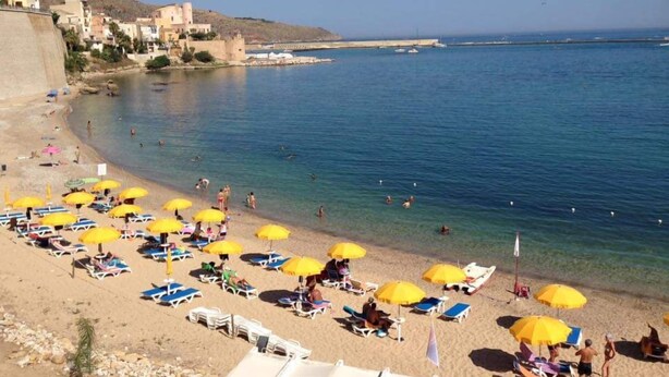 A beach with sun loungers and umbrellas, a clear blue sea, and buildings in the background. - Residence ITACA (Castellammare del Golfo)