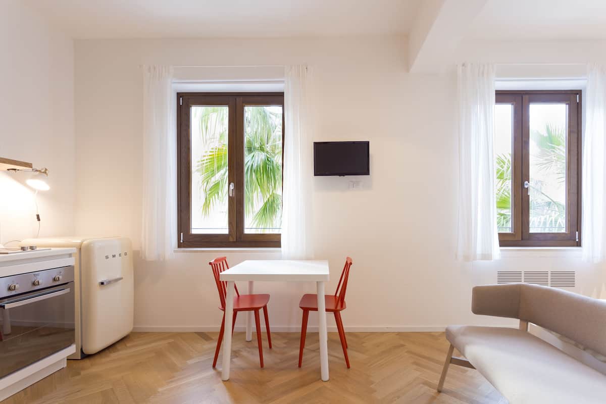Un espace de vie compact comprenant un coin cuisine, un coin repas avec une table et des chaises, un canapé et de grandes fenêtres avec des rideaux.