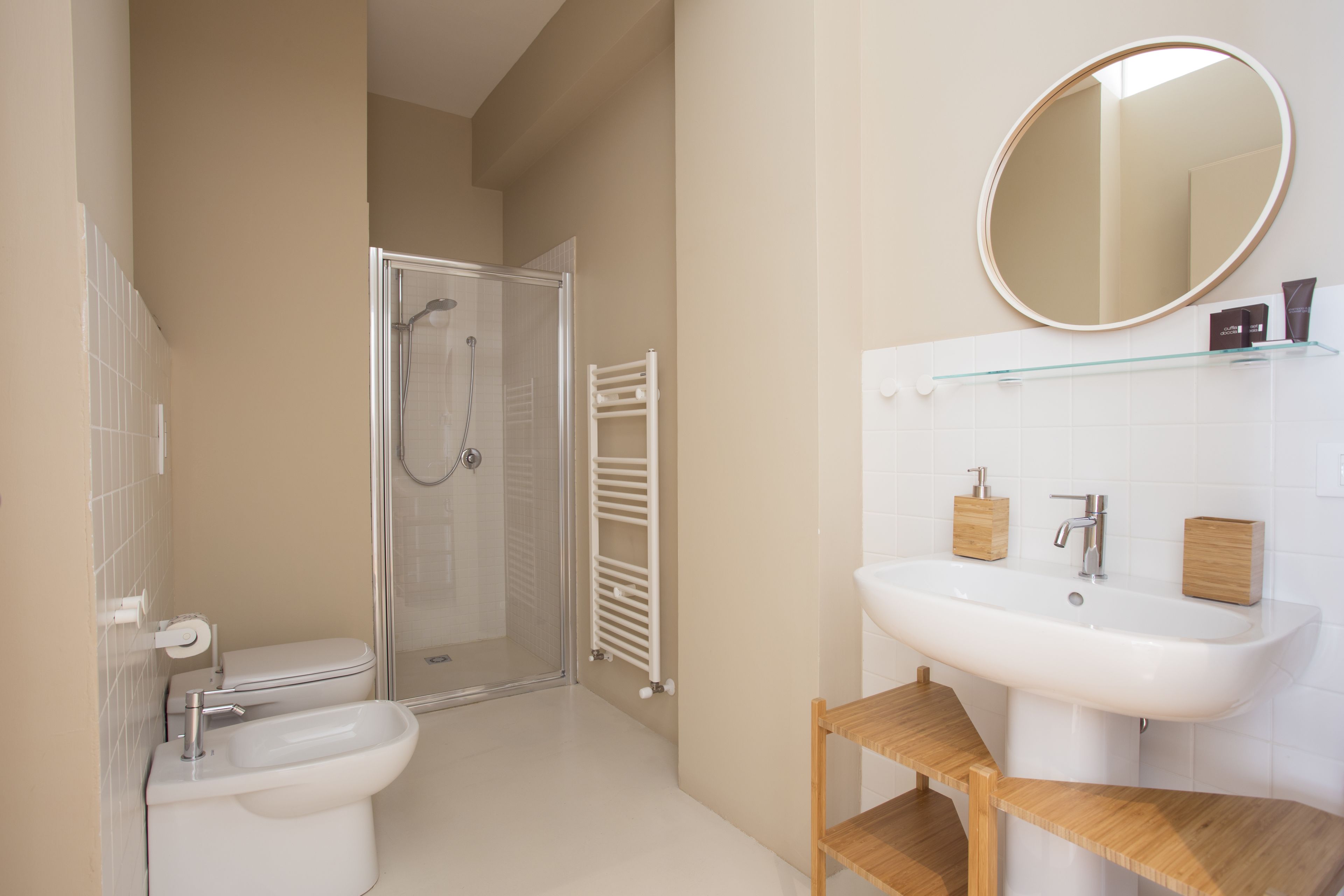 Un baño moderno con inodoro, bidé, cabina de ducha de vidrio, lavabo blanco y tocador de madera.