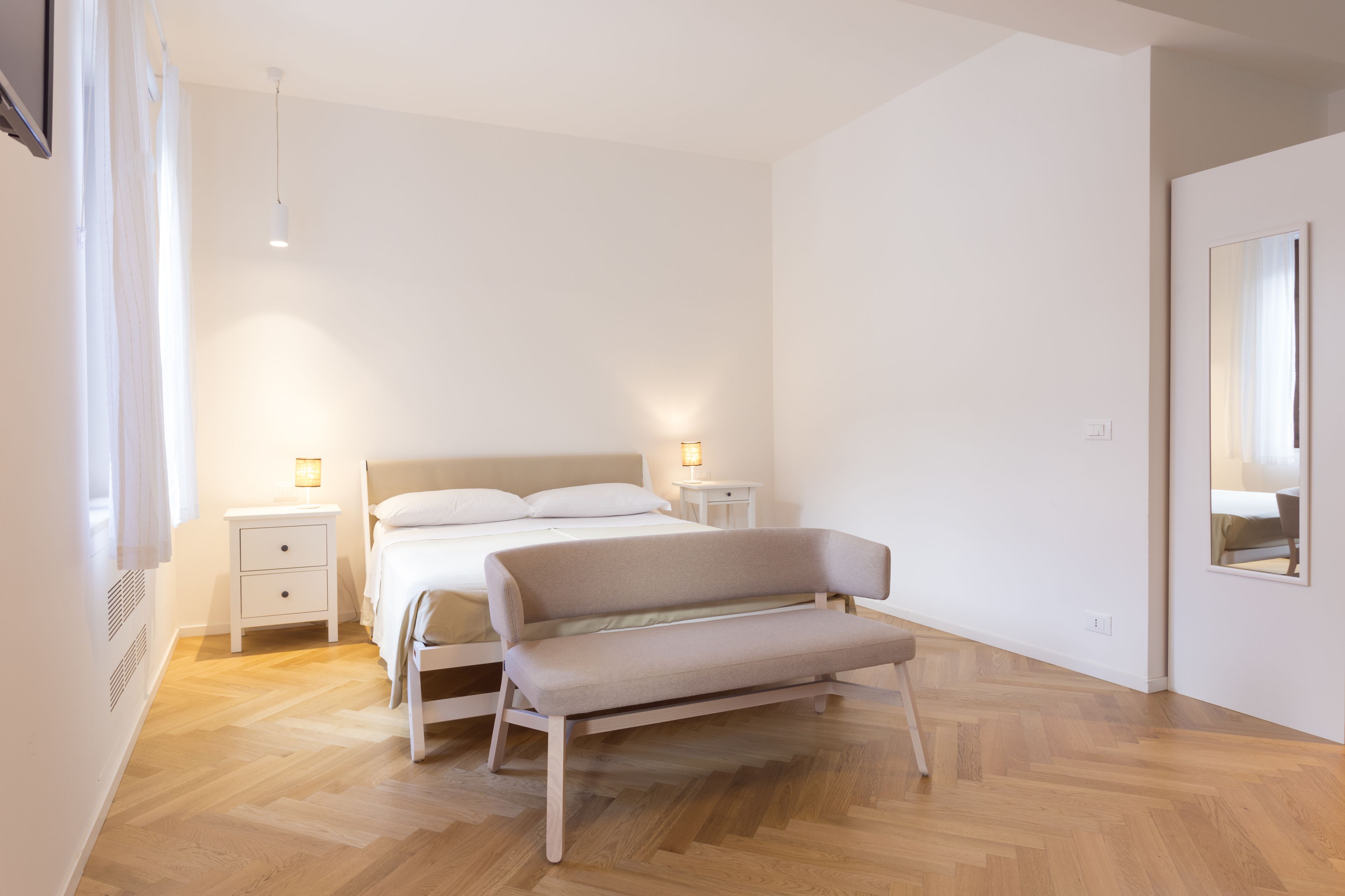 Un dormitorio moderno con una cama, mesitas de noche, un banco y un espejo.