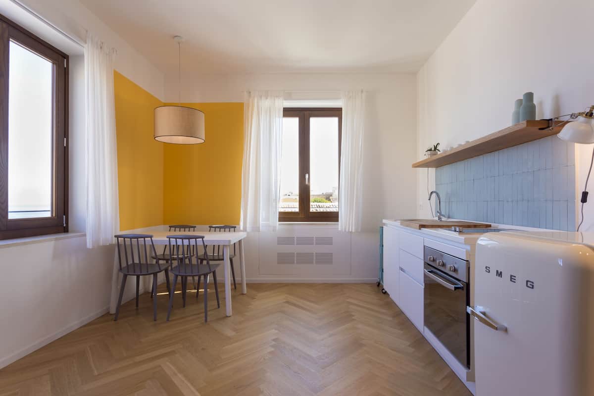 Une cuisine compacte avec un coin repas, un réfrigérateur blanc et une fenêtre avec des rideaux.