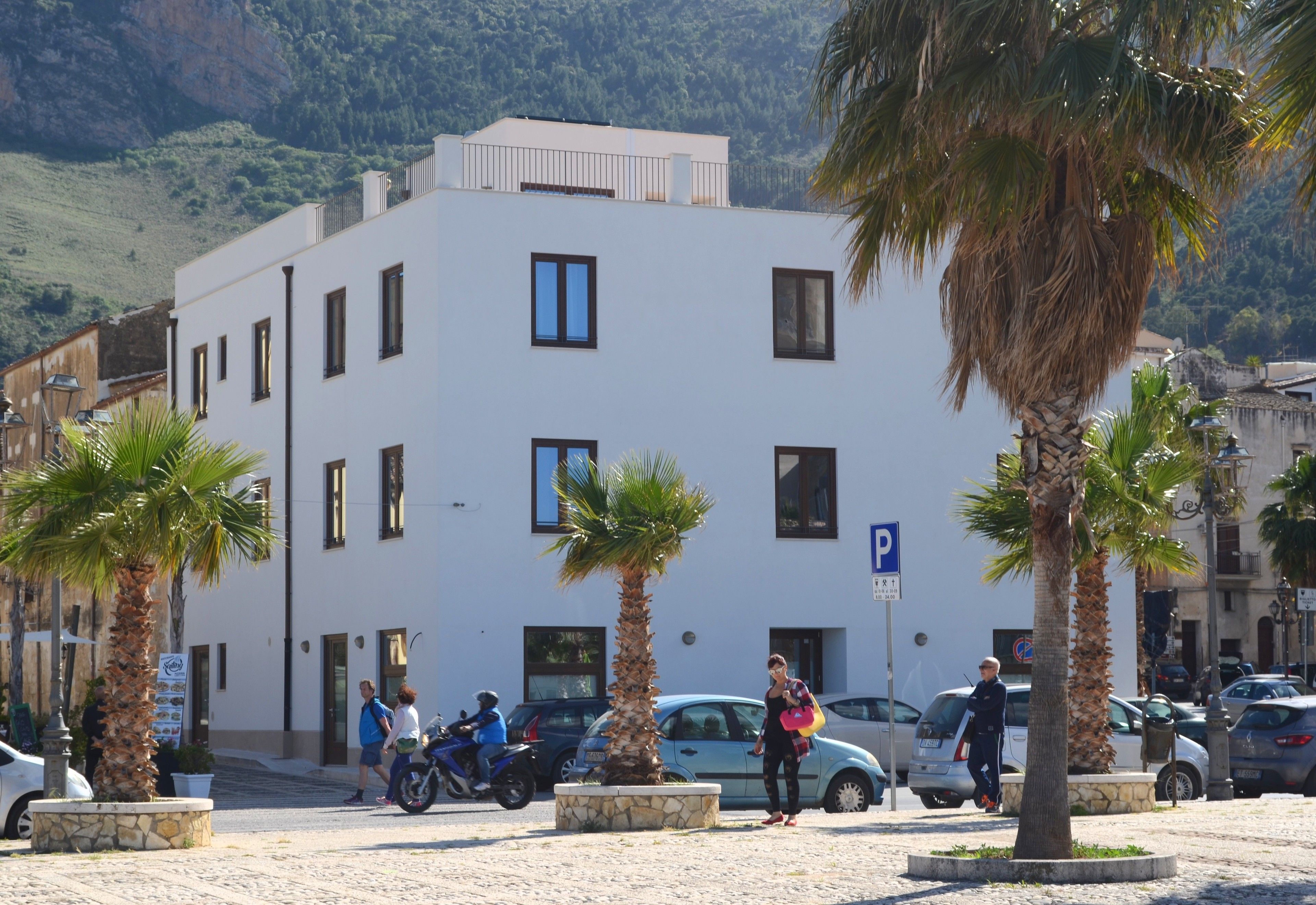 A modern building with a flat facade, multiple windows, and a parking sign.
