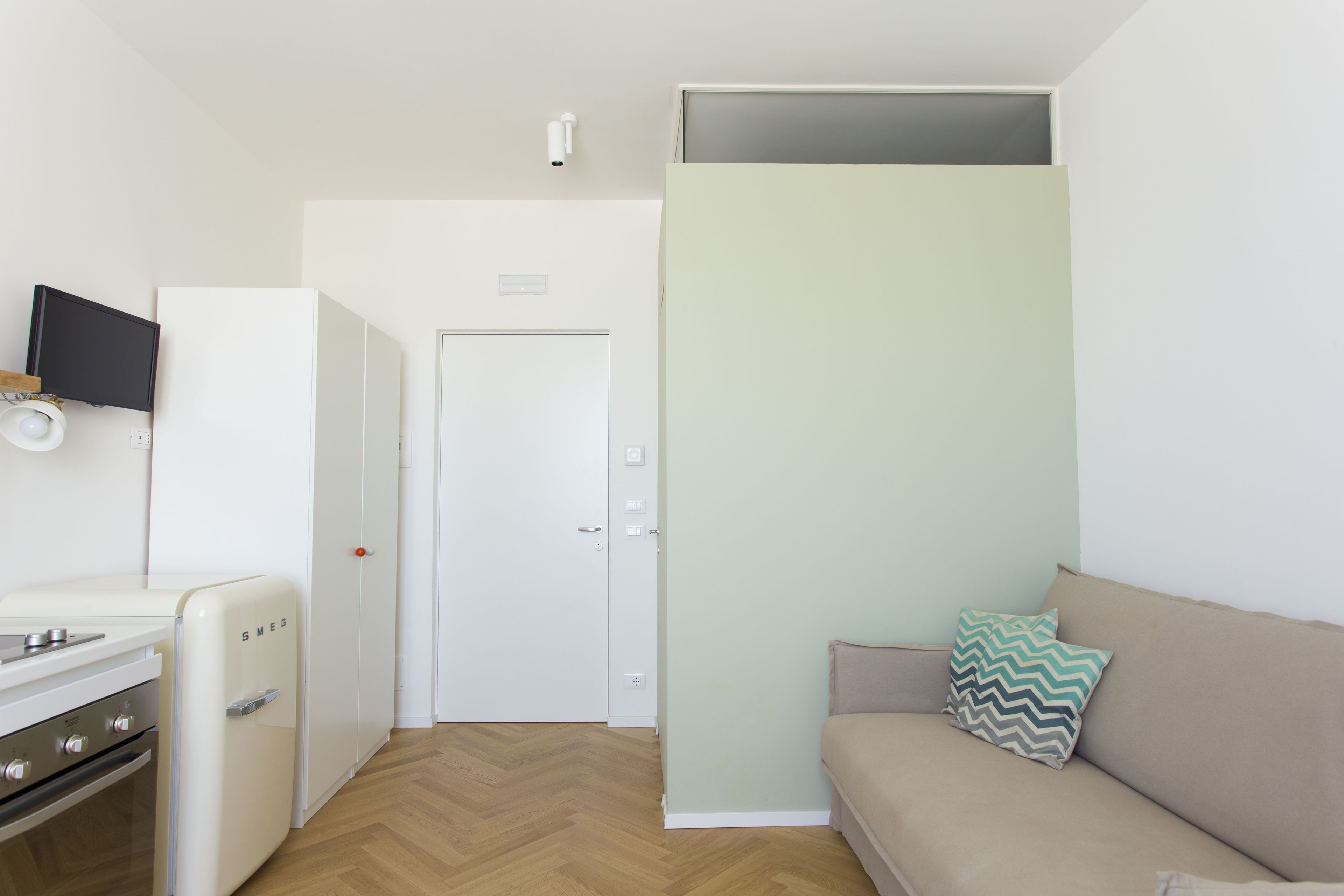 A compact living space with a kitchenette, a sofa, and a television mounted on the wall.