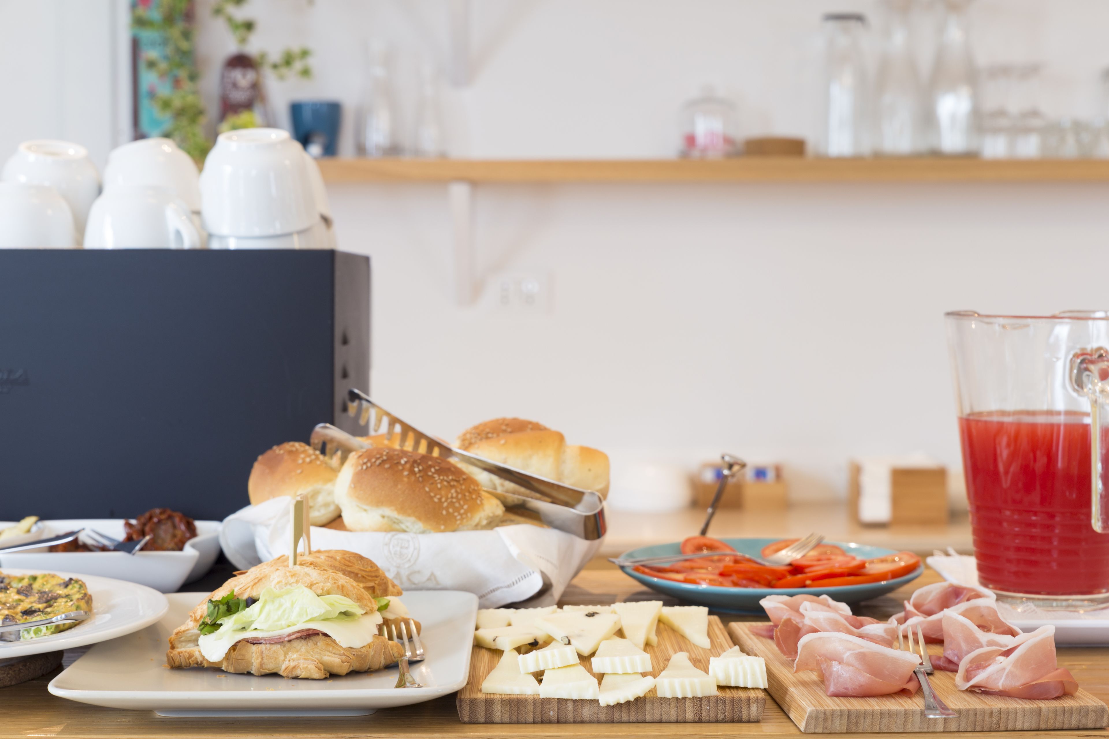 A table with various food items including sandwiches, cheese, and meat, along with a pitcher of red drink.