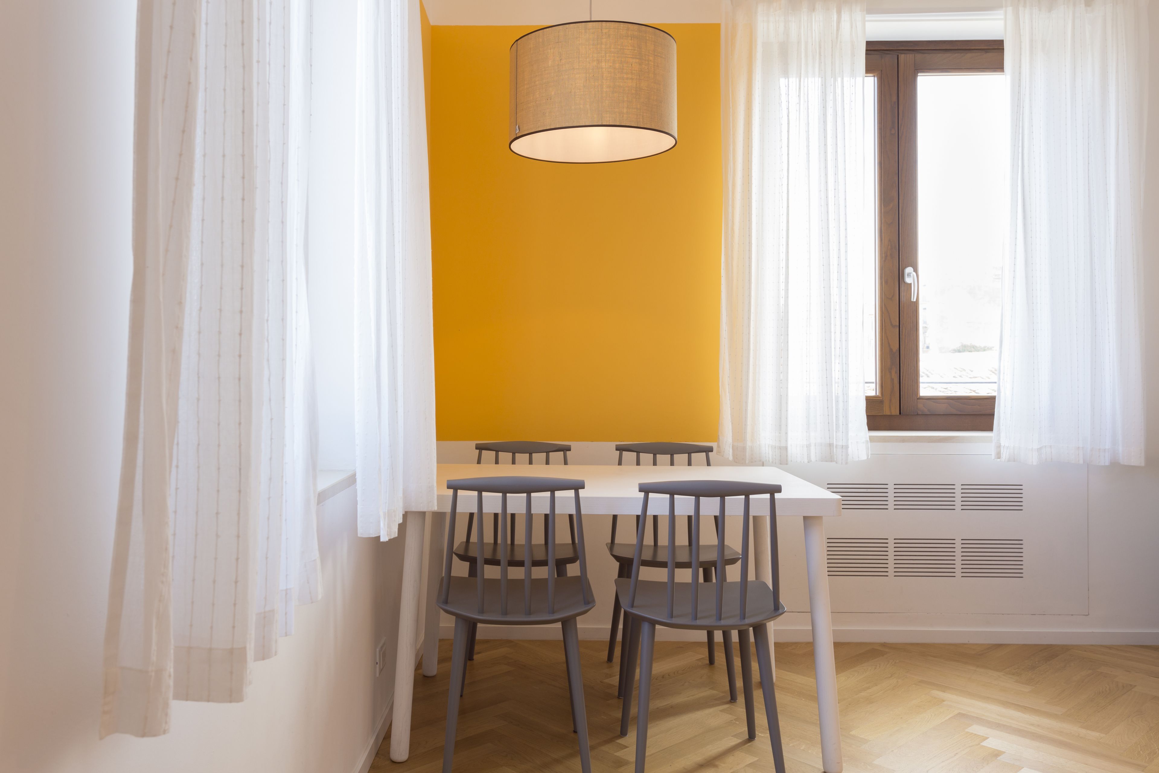 Un comedor con una mesa blanca y cuatro sillas, una lámpara colgante y una ventana con cortinas blancas.