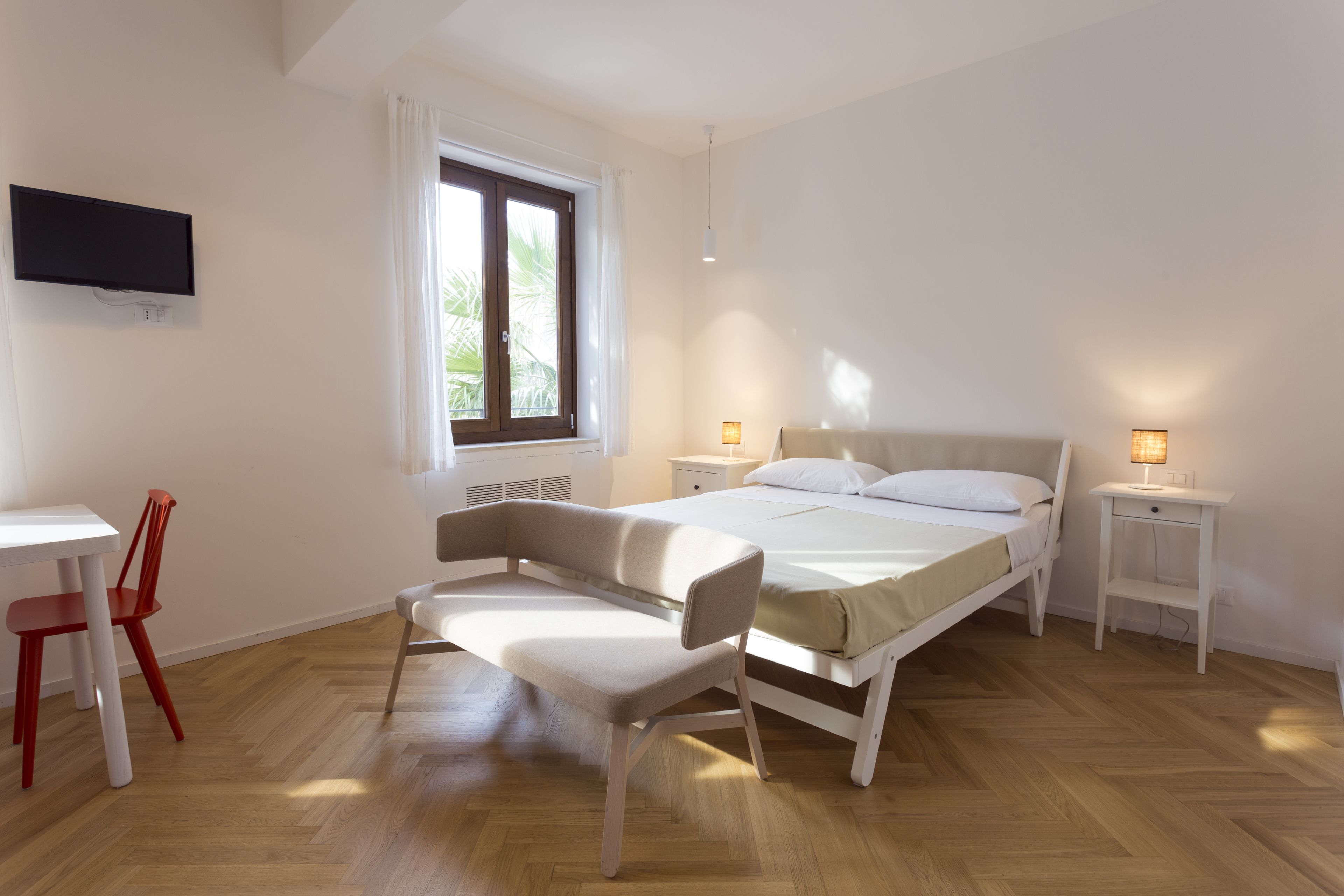 A bedroom with a bed, bedside tables, a chair, a desk, and a TV.